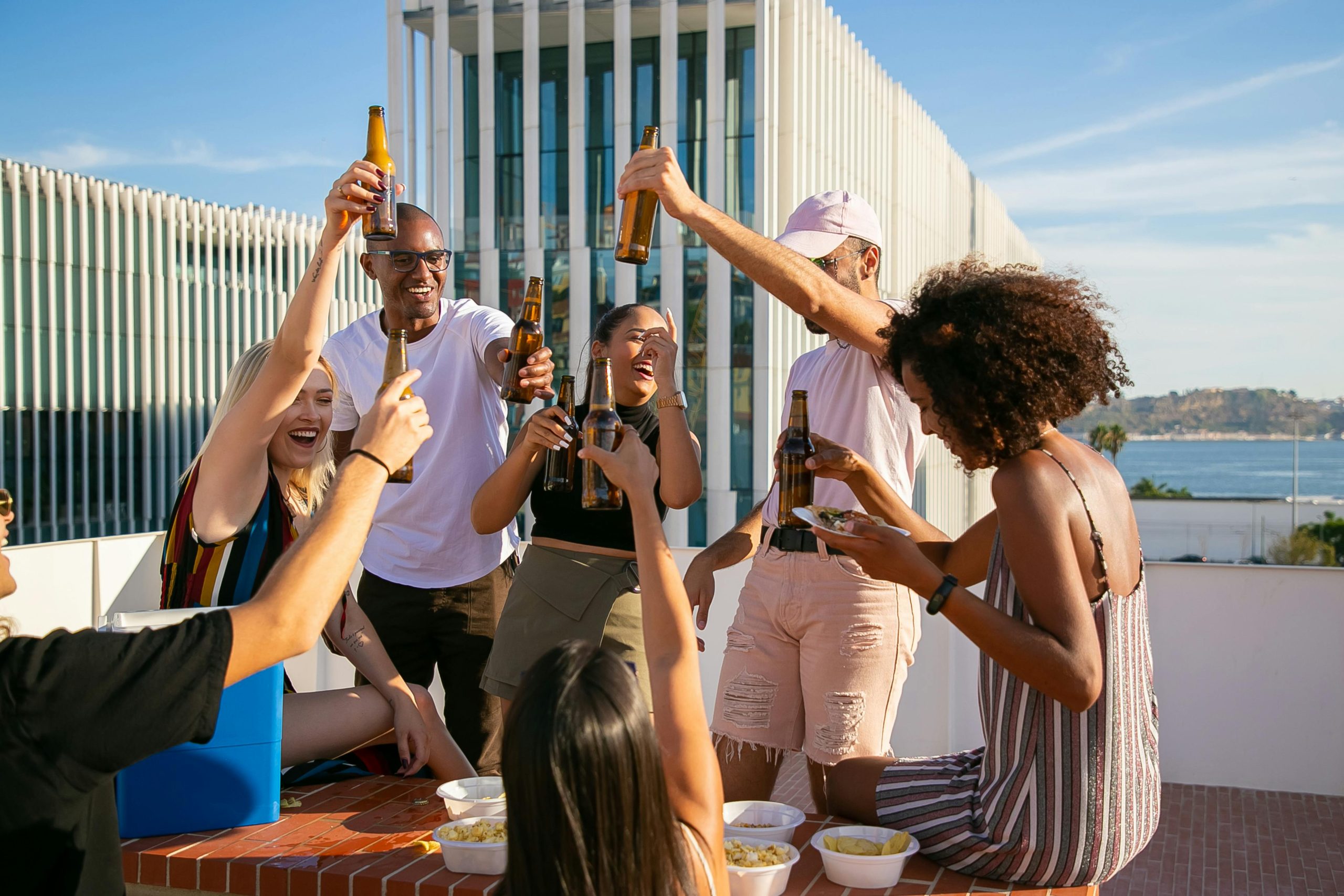 Group of friends enjoying a vibrant rooftop party, clinking beer bottles in celebration.